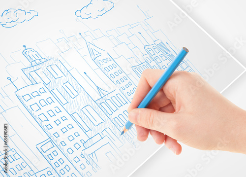 Photo: A person drawing sketch of a city with balloons and clouds on a A person drawing sketch of a city with balloons and clouds on a