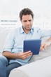 Handsome man sitting on the sofa using his tablet pc Handsome man sitting on the sofa using his tablet pc