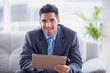 Businessman sitting on sofa using his tablet smiling at camera Businessman sitting on sofa using his tablet smiling at camera