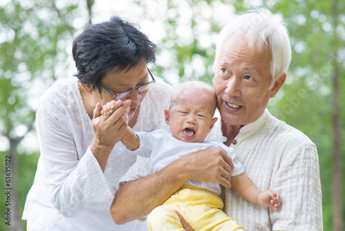Photo: Asian crying baby comforted by grandparents at outdoor garden Asian crying baby comforted by grandparents at outdoor garden