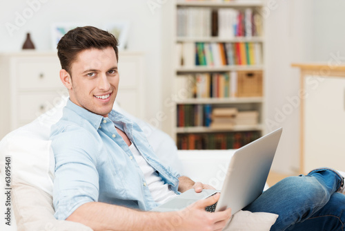 Photo: mann sitzt auf dem sofa mit seinem notebook mann sitzt auf dem sofa mit seinem notebook