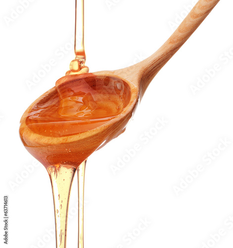 Photo: Honey dripping from a wooden honey dipper isolated on white back Honey dripping from a wooden honey dipper isolated on white back