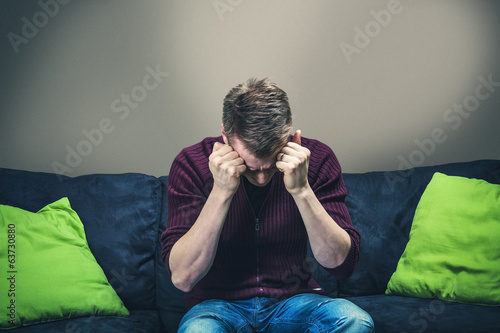 Photo: Man sitting on sofa looking painful Man sitting on sofa looking painful