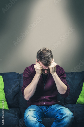 Photo: Man sitting on sofa looking painful Man sitting on sofa looking painful