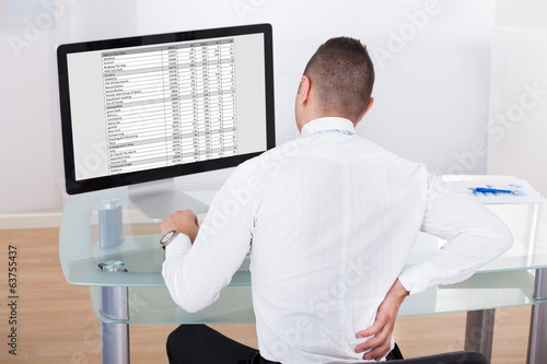 Photo: Businessman With Backache Using Computer At Desk Businessman With Backache Using Computer At Desk