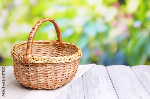 Photo: Empty wicker basket on wooden table, on bright background Empty wicker basket on wooden table, on bright background