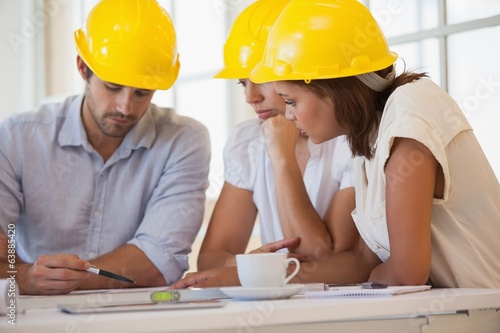 Photo: Architects in yellow helmets working on blueprints Architects in yellow helmets working on blueprints