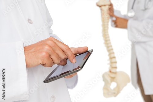Photo: Mid section of doctors with digital table and skeleton model Mid section of doctors with digital table and skeleton model