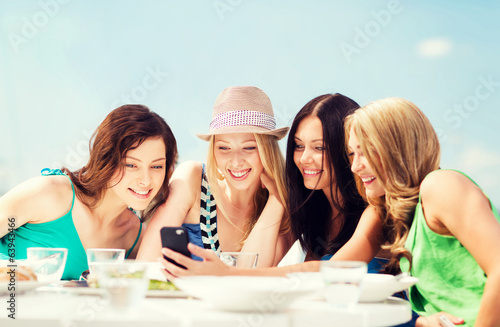 Photo: girls looking at smartphone in cafe on the beach girls looking at smartphone in cafe on the beach