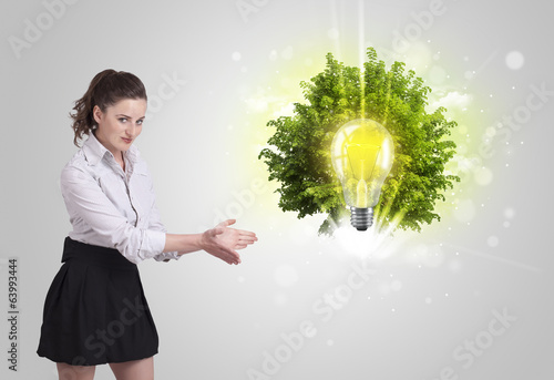 Photo: Young girl presenting idea light bulb with green tree Young girl presenting idea light bulb with green tree