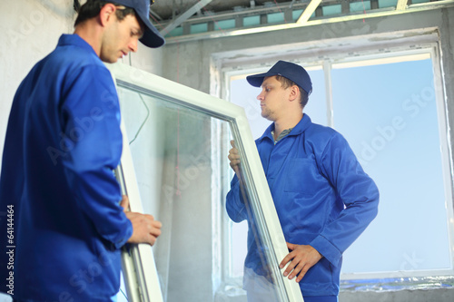 Photo: Two workers in blue work clothes set a new window Two workers in blue work clothes set a new window