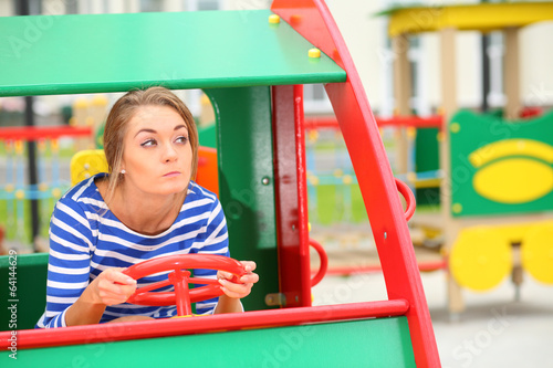 Photo: Funny girl sitting in a toy car on the playground Funny girl sitting in a toy car on the playground
