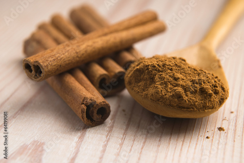 Photo: Cinnamon, whole sticks behind wooden spoon with a heap of powder Cinnamon, whole sticks behind wooden spoon with a heap of powder