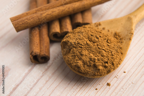 Photo: Cinnamon, whole sticks behind wooden spoon with a heap of powder Cinnamon, whole sticks behind wooden spoon with a heap of powder
