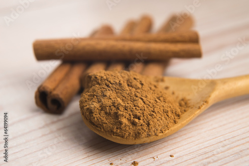 Photo: Cinnamon, whole sticks behind wooden spoon with a heap of powder Cinnamon, whole sticks behind wooden spoon with a heap of powder