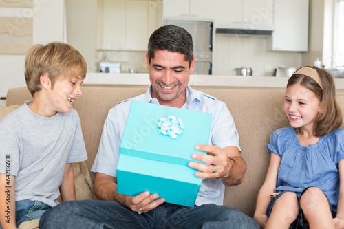 Photo: Father opening gift given by children on sofa Father opening gift given by children on sofa