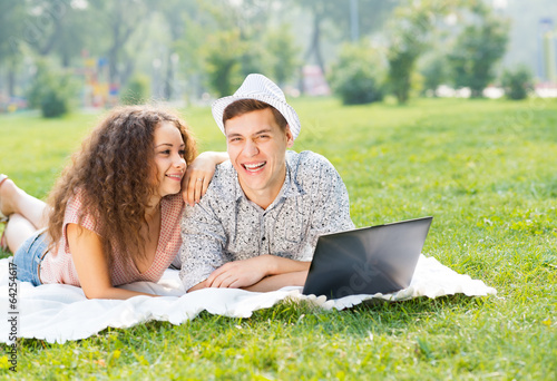 Photo: couple lying together in a park with laptop couple lying together in a park with laptop