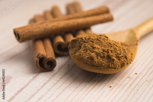 Photo: Cinnamon, whole sticks behind wooden spoon with a heap of powder Cinnamon, whole sticks behind wooden spoon with a heap of powder