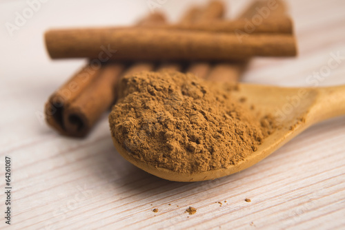 Photo: Cinnamon, whole sticks behind wooden spoon with a heap of powder Cinnamon, whole sticks behind wooden spoon with a heap of powder