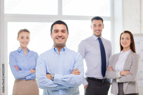 Photo: smiling businessman in office with team on back smiling businessman in office with team on back