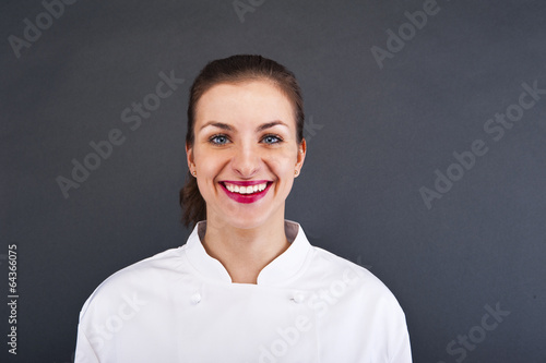 Photo: Close-up woman cook look round or hear something, over gray wall Close-up woman cook look round or hear something, over gray wall