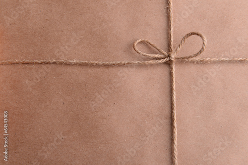 Photo: String tied in bow on brown paper packaging close-up String tied in bow on brown paper packaging close-up