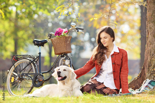Photo: Beautiful female sitting on a grass with her dog in a park Beautiful female sitting on a grass with her dog in a park
