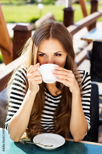 Photo: Young woman drinking coffee in a cafe outdoors Young woman drinking coffee in a cafe outdoors