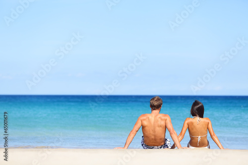 Photo: Couple on beach sitting in sand looking at sea Couple on beach sitting in sand looking at sea