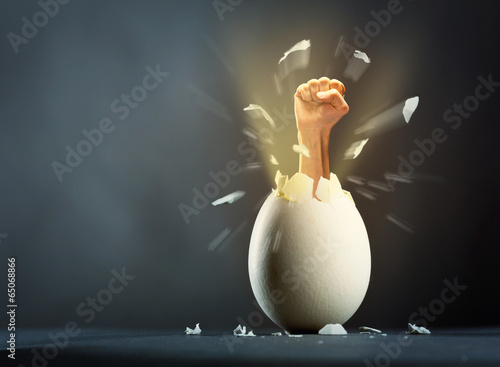 Photo: Broken egg with hand isolated on gray background Broken egg with hand isolated on gray background