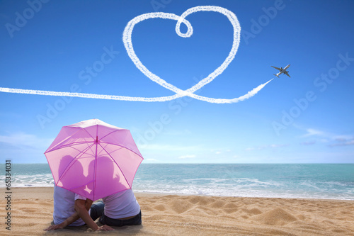 Photo: young couple romantic kissing at the beach with the umbrella young couple romantic kissing at the beach with the umbrella
