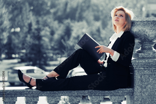 Photo: Young business woman with a folder sitting on the banister Young business woman with a folder sitting on the banister