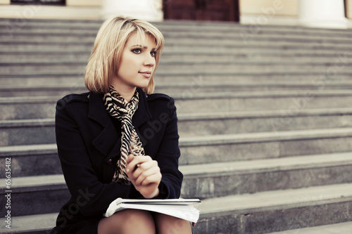 Photo: Young business woman with notebook sitting on the steps Young business woman with notebook sitting on the steps
