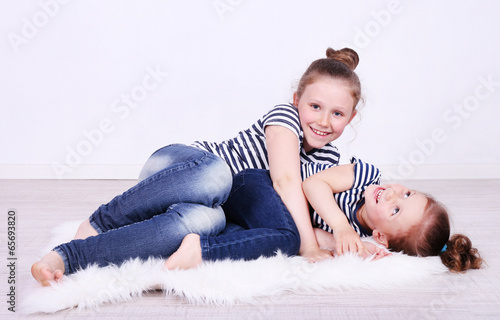 Photo: Beautiful small girls lying on floor on wall background Beautiful small girls lying on floor on wall background