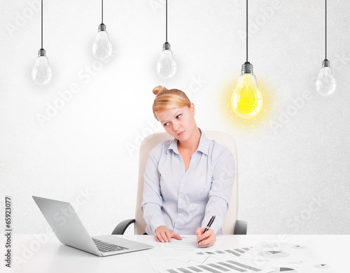 Photo: Business woman sitting at table with idea light bulbs Business woman sitting at table with idea light bulbs