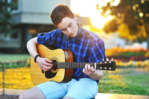 Photo: Young man playing on acoustic guitar in park Young man playing on acoustic guitar in park