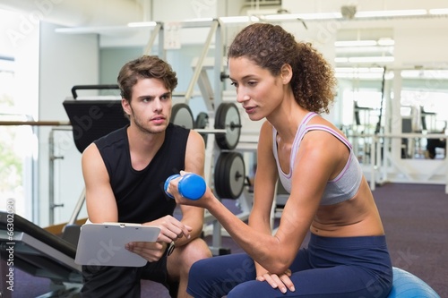 Photo: Trainer watching client lift dumbbells on exercise ball Trainer watching client lift dumbbells on exercise ball