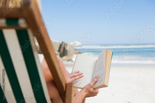 Photo: Woman sitting in deck chair at the beach reading Woman sitting in deck chair at the beach reading