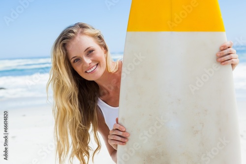 Photo: Blonde surfer holding her board smiling at camera Blonde surfer holding her board smiling at camera