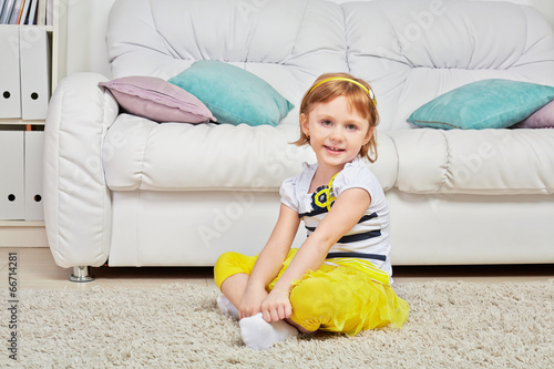Photo: Smiling little girl sits on light carpet in room Smiling little girl sits on light carpet in room