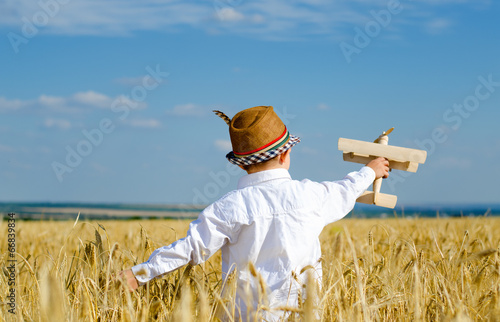 Photo: Cute little boy flying a toy plane in a wheatfield Cute little boy flying a toy plane in a wheatfield