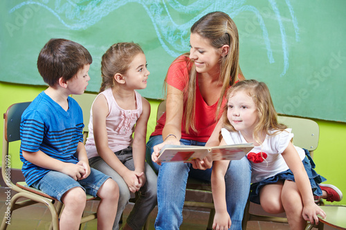 Photo: Child care worker and children reading book in kindergarten Child care worker and children reading book in kindergarten