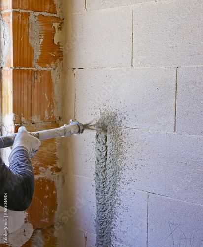 Photo: Worker performs internal plaster with machine applying plaster Worker performs internal plaster with machine applying plaster