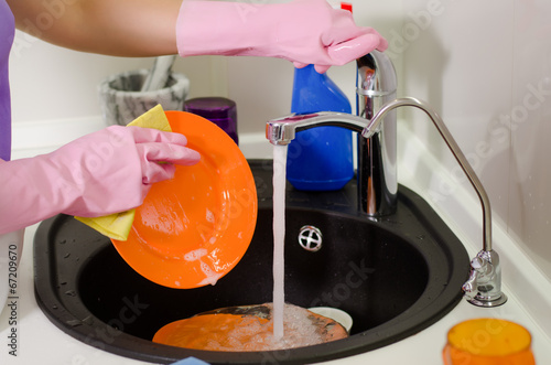 Photo: Woman rinsing plates under the tap Woman rinsing plates under the tap