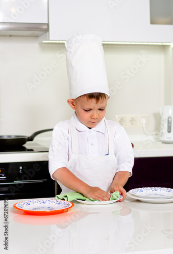 Photo: Cute young chef checking his dinner plates Cute young chef checking his dinner plates