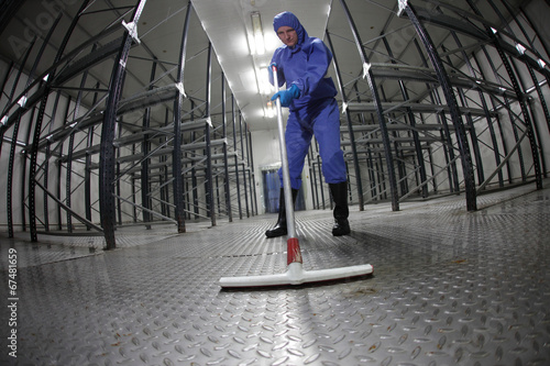 Photo: worker in uniform cleaning floor in empty storehouse worker in uniform cleaning floor in empty storehouse
