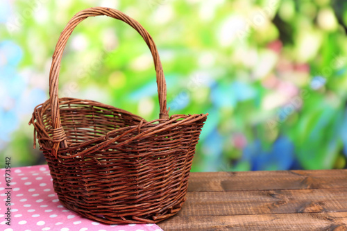 Photo: Empty wicker basket on wooden table, on bright background Empty wicker basket on wooden table, on bright background