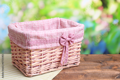 Photo: Empty wicker basket on wooden table, on bright background Empty wicker basket on wooden table, on bright background