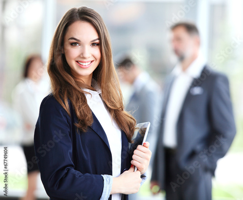 Photo: Business woman standing in foreground with a tablet in her hands Business woman standing in foreground with a tablet in her hands