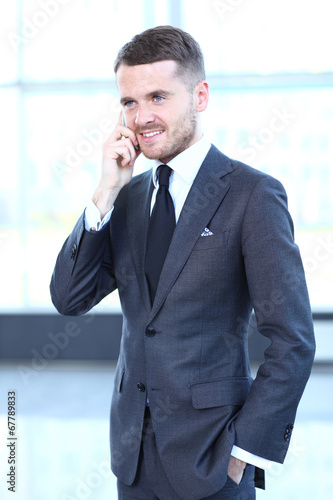 Photo: A young handsome business man on phone at office building A young handsome business man on phone at office building